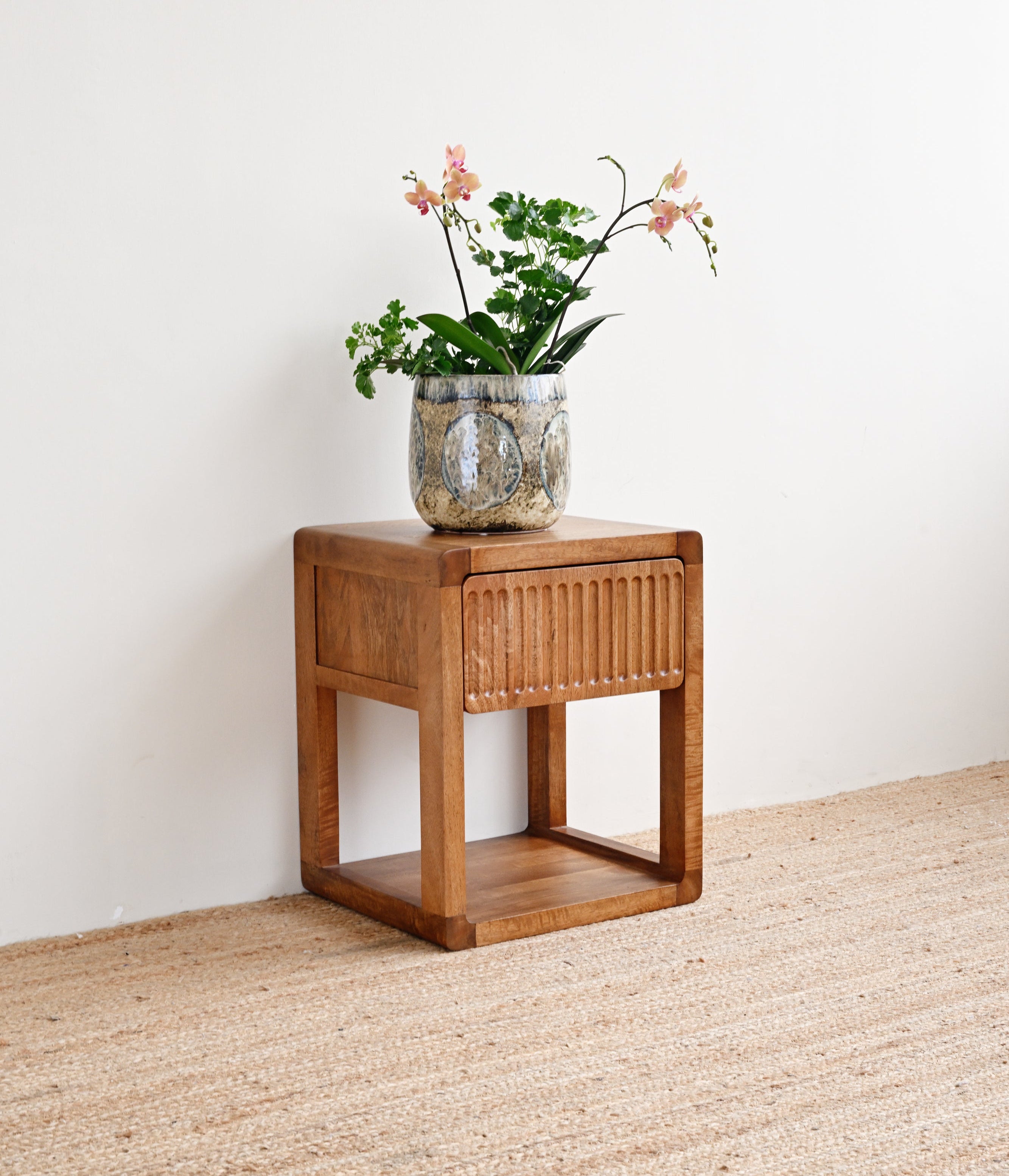 Wooden side table with a vase of flowers on a beige carpet against a white wall