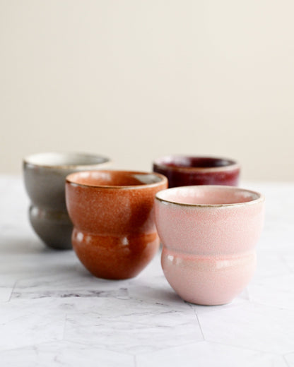 Four ceramic cups in different colors on a marble surface with a light background