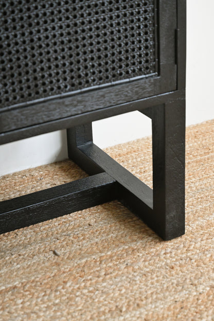 Close-up of a black rattan cabinet corner on a textured beige floor.