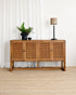 Wooden sideboard with rattan doors in a room with white curtains and a lamp.