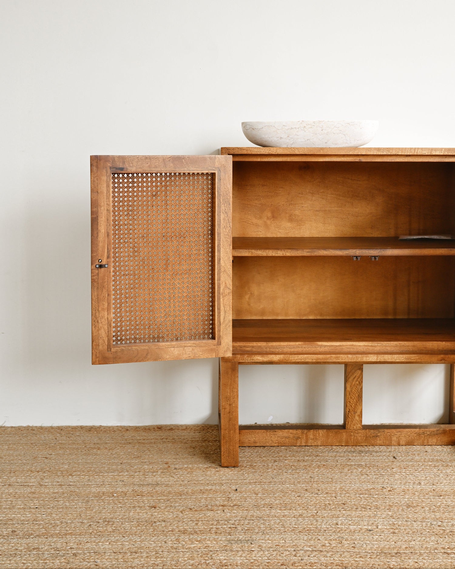 Wooden sideboard with a rattan door against a white wall.