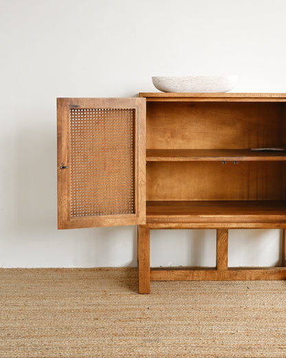 Wooden sideboard with a rattan door against a white wall.