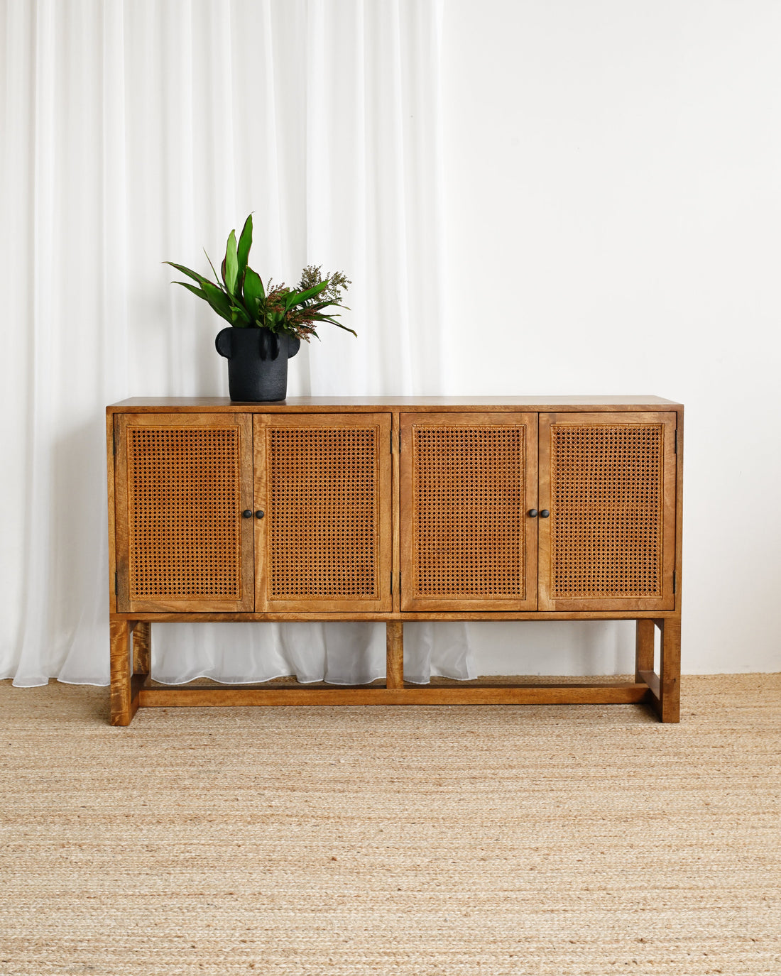 Wooden sideboard with rattan doors in a room with white curtains and a beige carpet.