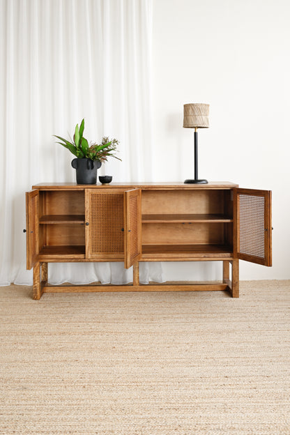 Wooden sideboard with open doors, potted plant, and lamp against a white curtain background.