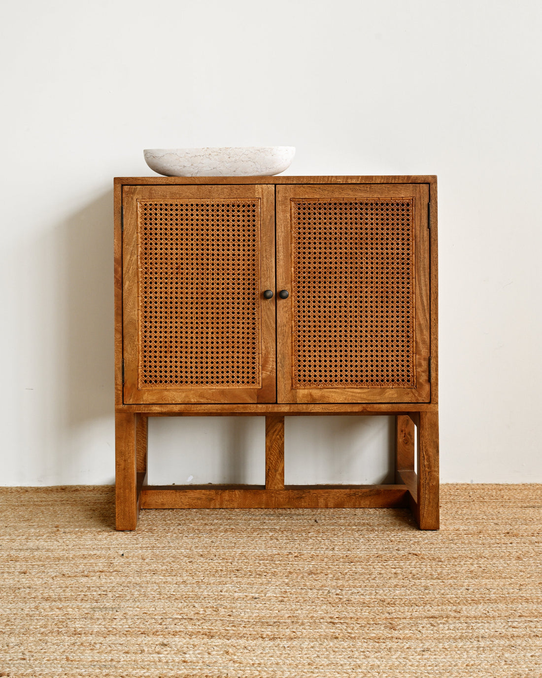Wooden cabinet with wicker doors on a beige carpet against a white wall