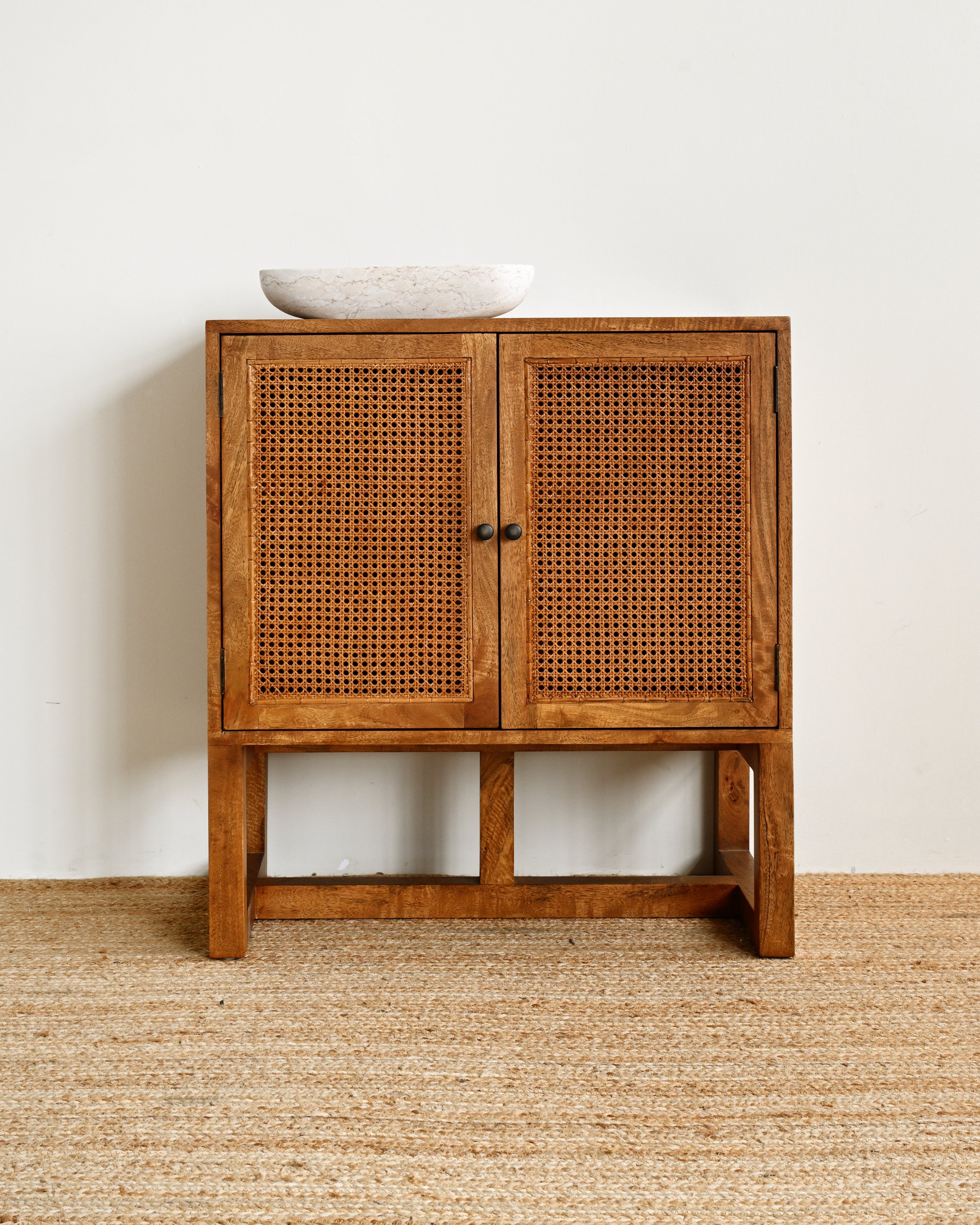 Wooden cabinet with wicker doors on a beige carpet against a white wall