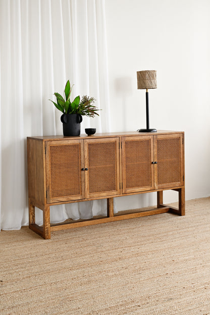 Wooden sideboard with rattan doors in a room with white curtains and a lamp.