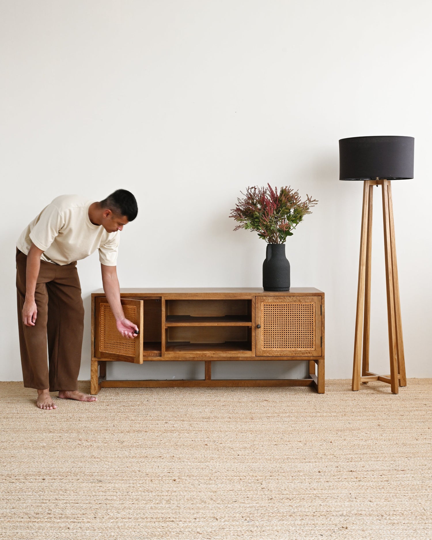 Person interacting with a wooden cabinet in a minimalistic room with a lamp and plant.