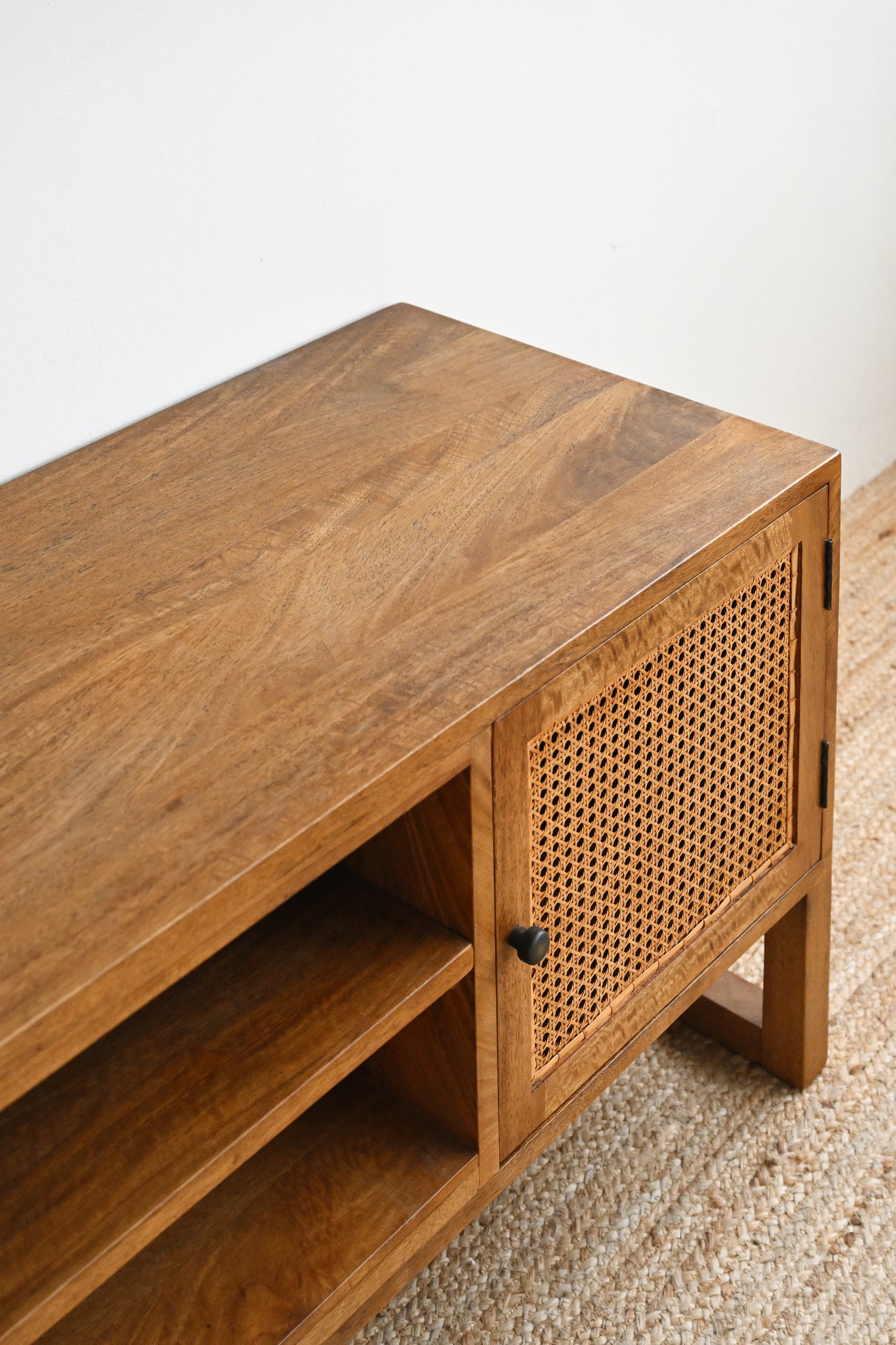 Wooden TV stand with rattan door on a carpeted floor