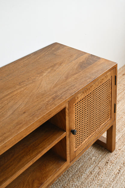 Wooden TV stand with rattan door on a carpeted floor