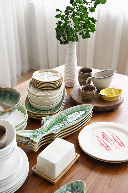 Collection of ceramic dishes on a wooden table with a plant in the background
