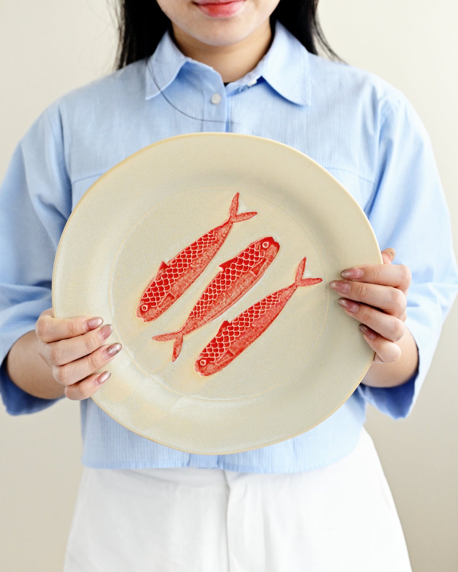 Person holding a plate with red fish illustrations against a plain background