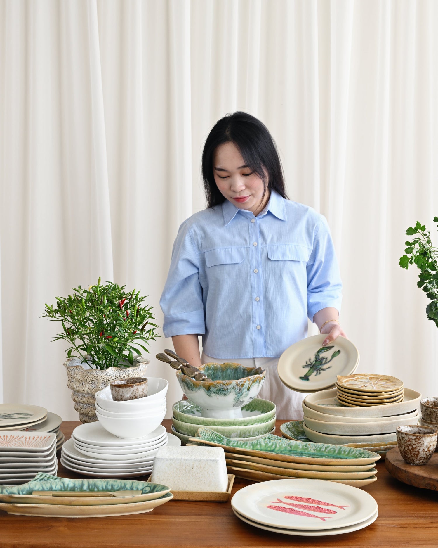 Woman in a light blue shirt standing behind a table with various ceramic plates and bowls.