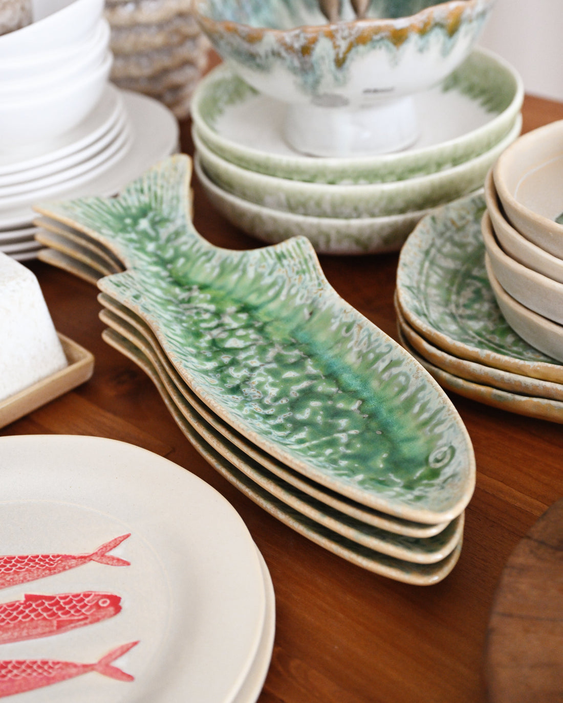 Set of ceramic plates including a fish-shaped platter on a wooden table.