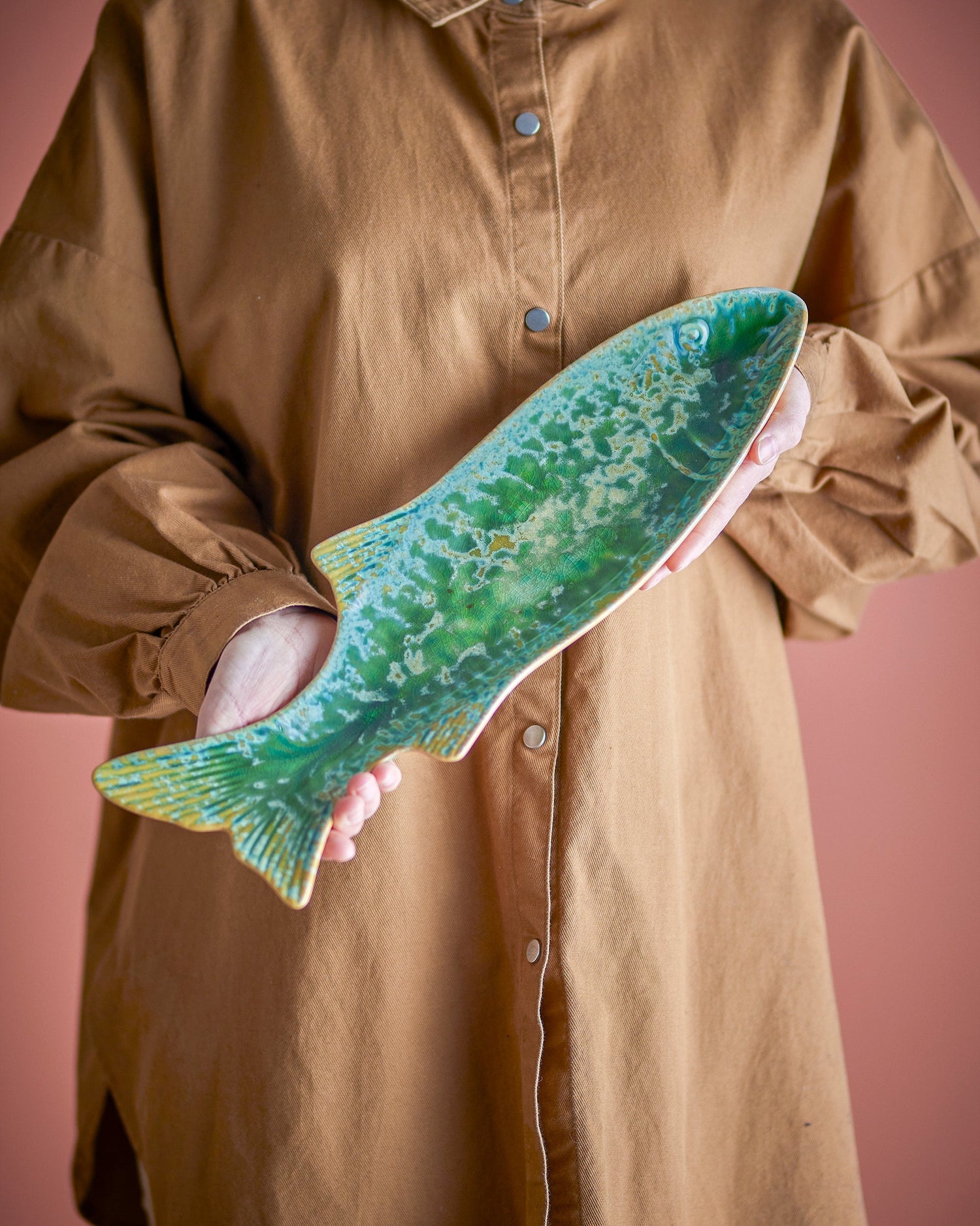 Person holding a large green fish against a pink background