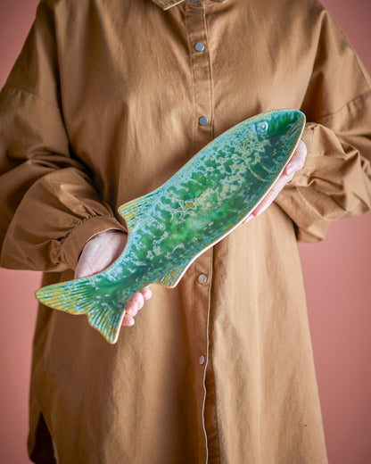 Person holding a large green fish against a pink background