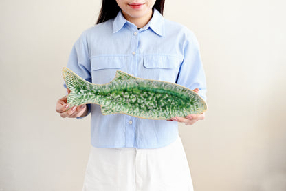 Person holding a large green ceramic fish against a plain background