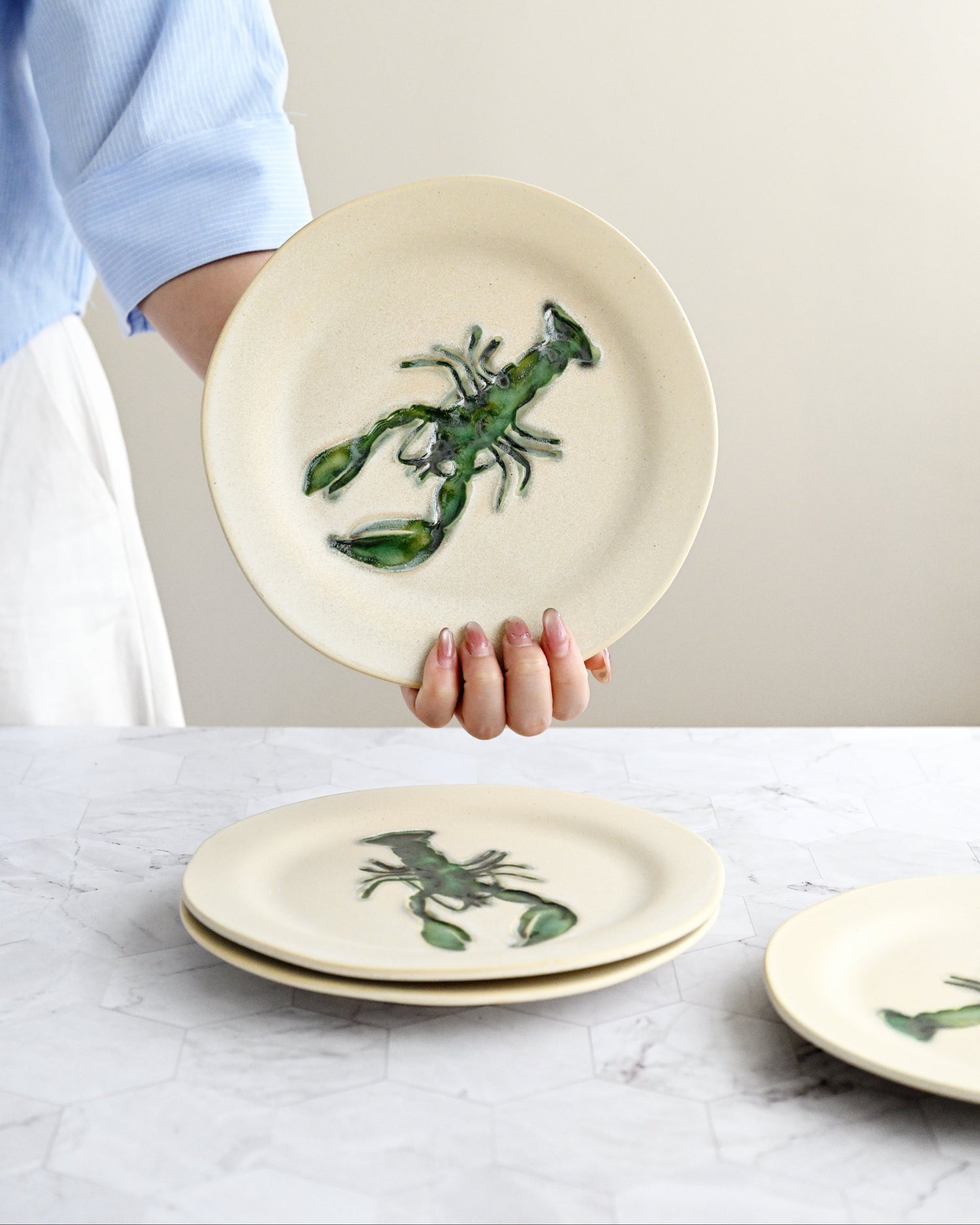 Person holding a ceramic plate with a green lobster design on a marble surface.