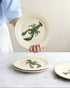 Person holding a ceramic plate with a green lobster design on a marble surface.