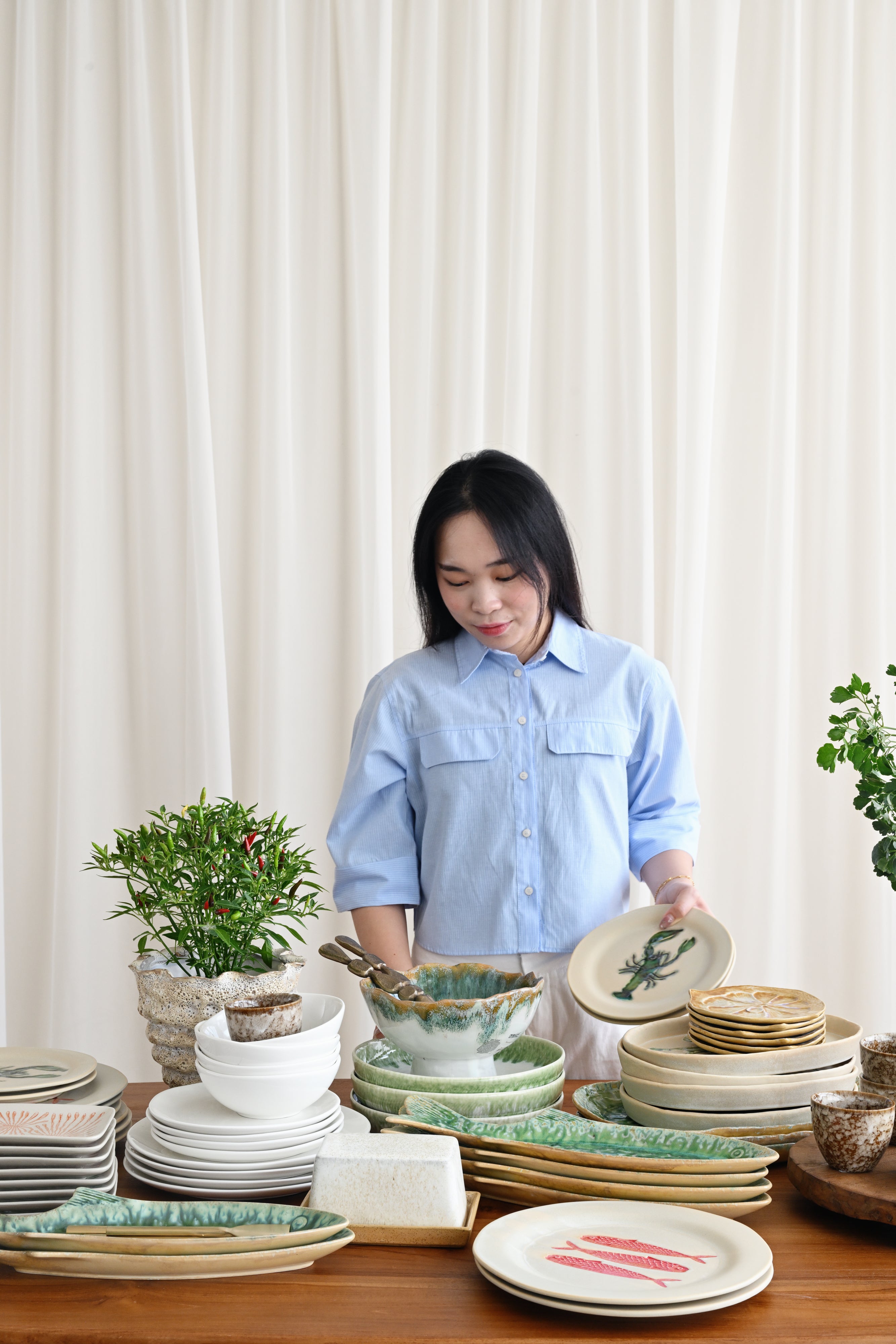 Woman in a light blue shirt standing behind a table with various ceramic plates and bowls.