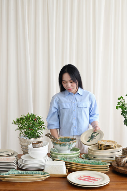 Woman in a light blue shirt standing behind a table with various ceramic plates and bowls.