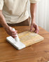 Person using a white kitchen tool on a wooden cutting board