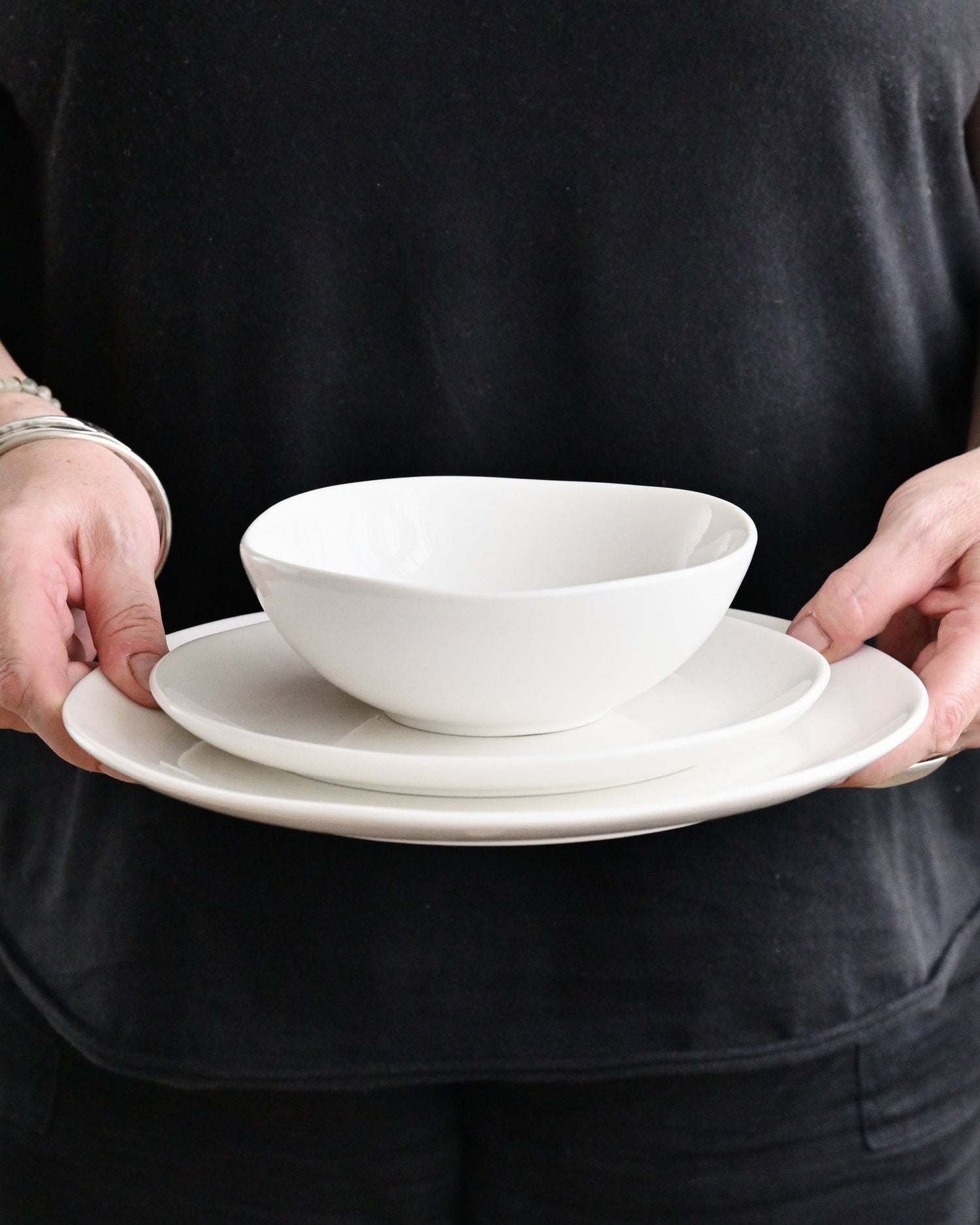 Person holding a white bowl and plate set against a neutral background