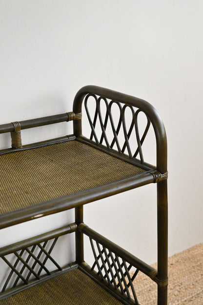Rattan bar cart with woven seat and shelves against a white wall.