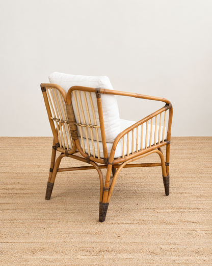 Rattan armchair with white cushion on a wooden floor and light-colored wall background
