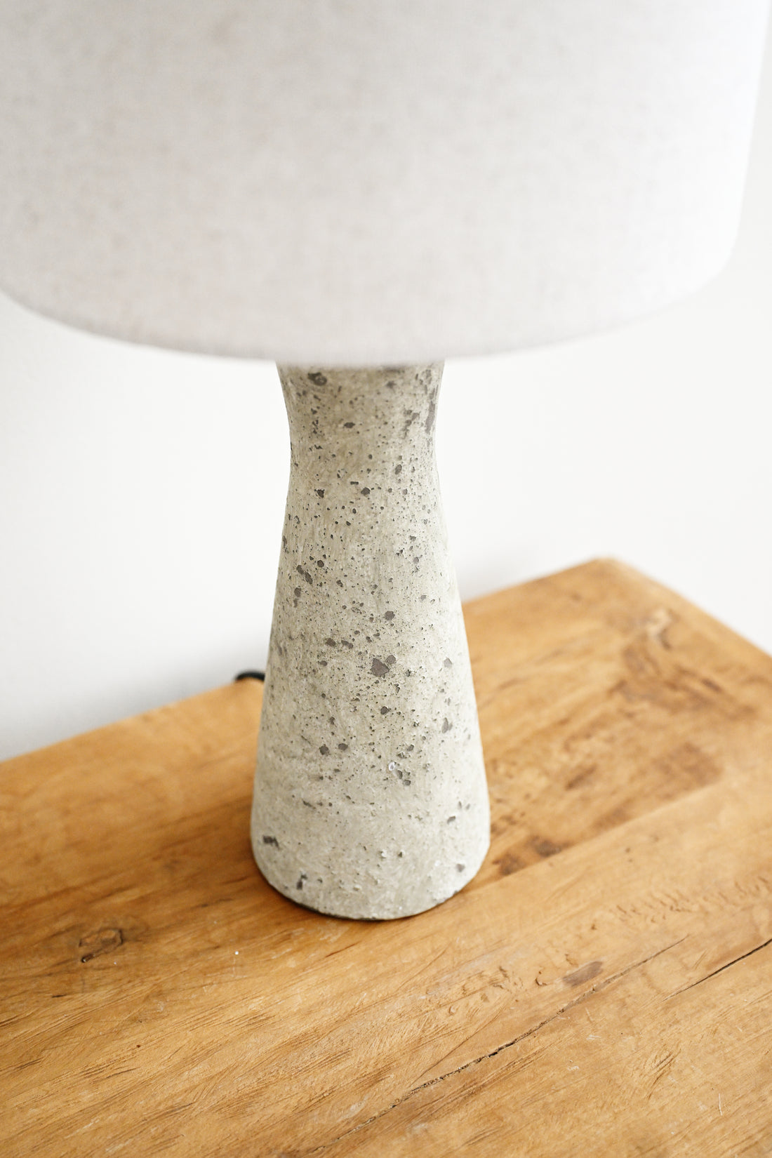 Table lamp with a white shade and speckled gray base on a wooden surface.
