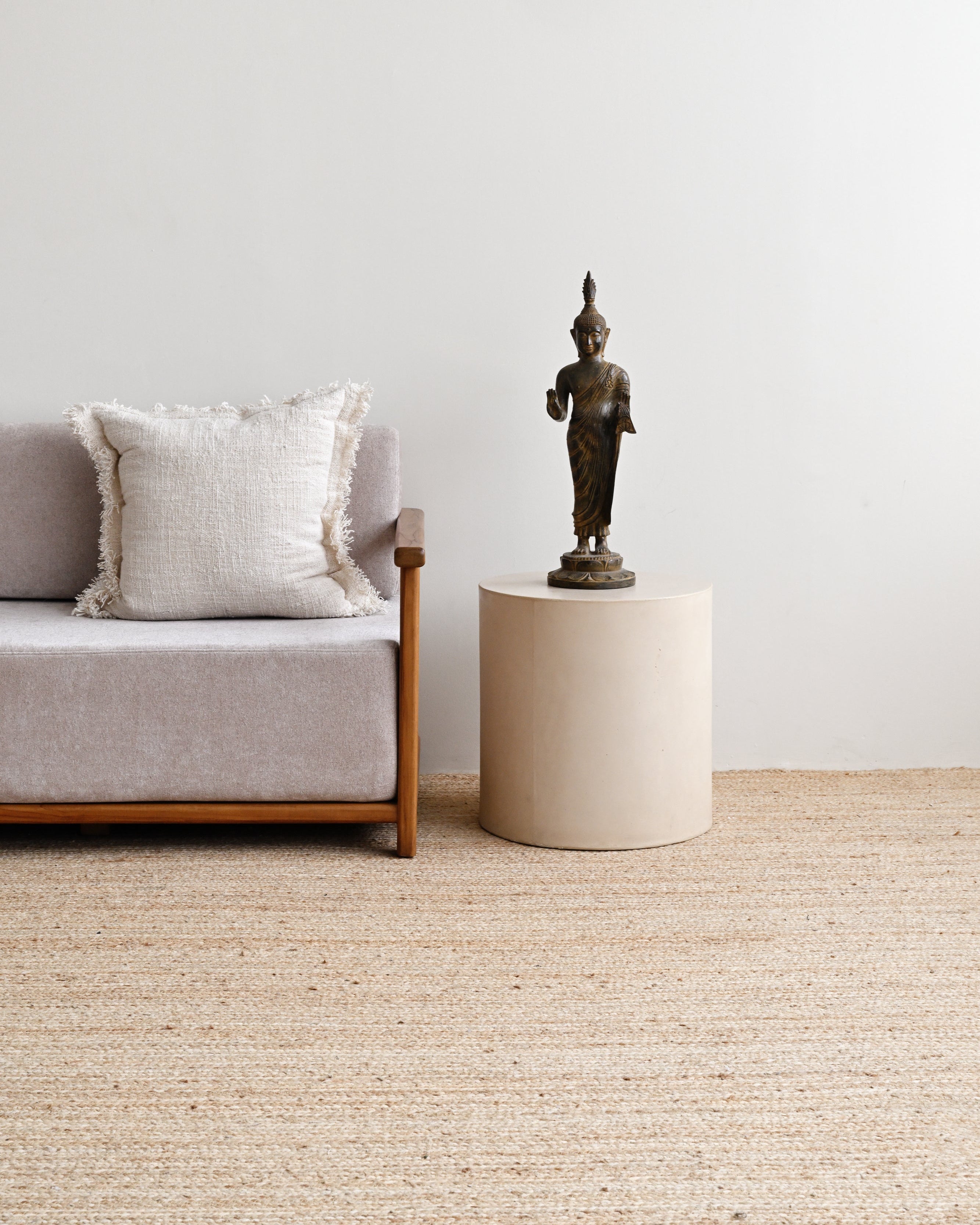 Sofa with a pillow and a small table with a statue on a light-colored carpet.