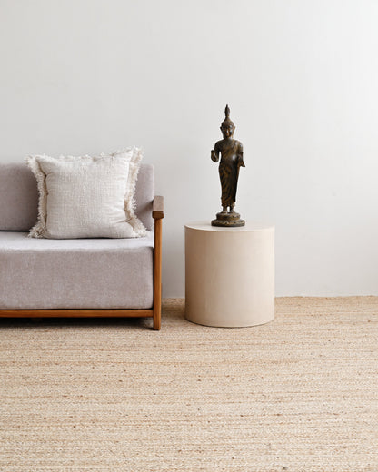 Sofa with a pillow and a small table with a statue on a light-colored carpet.