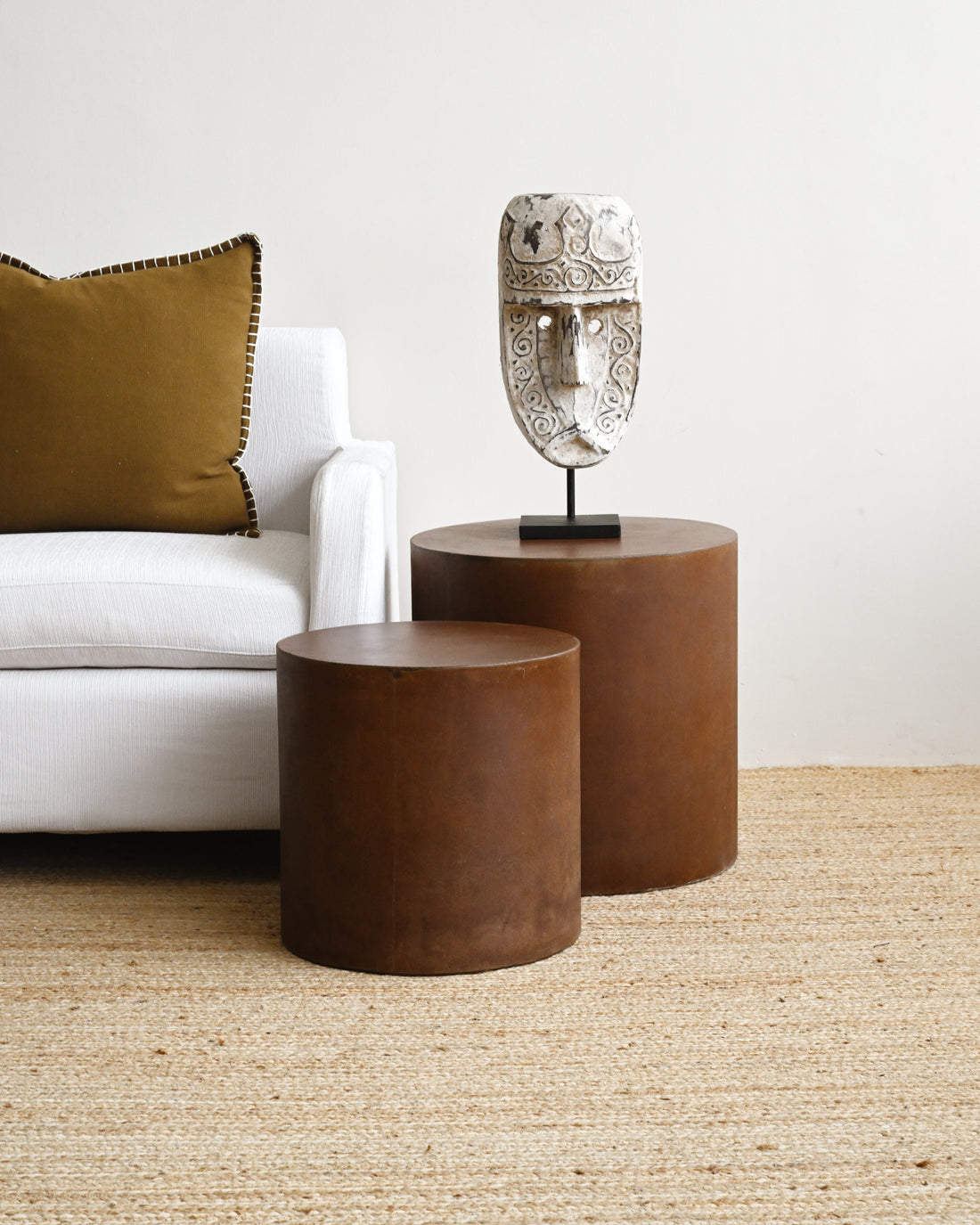 Two brown side tables with a decorative mask on a light-colored rug.