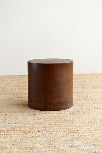 Brown cylindrical stool on a textured surface with a neutral background