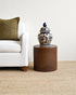 Vase on a small round wooden table next to a white sofa with a green pillow.