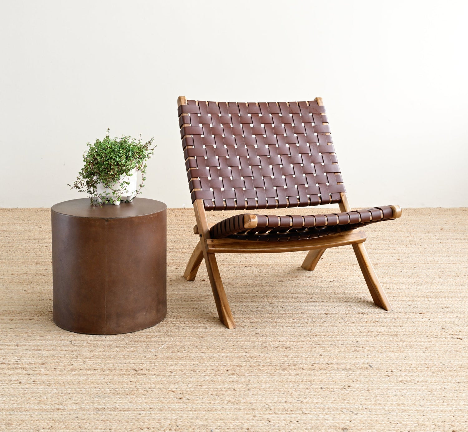 Brown woven chair and round wooden table on a light wood floor with a white wall background