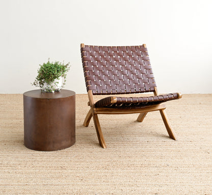 Brown woven chair and round wooden table on a light wood floor with a white wall background