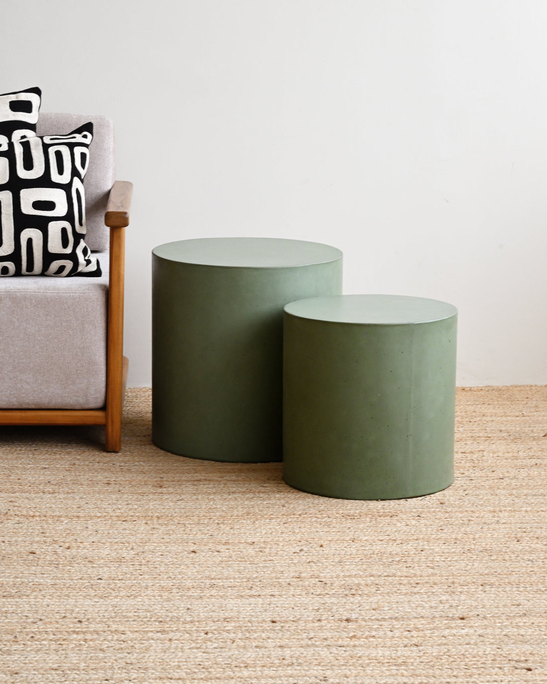 Two green cylindrical stools in front of a gray sofa with a patterned cushion on a beige carpet.