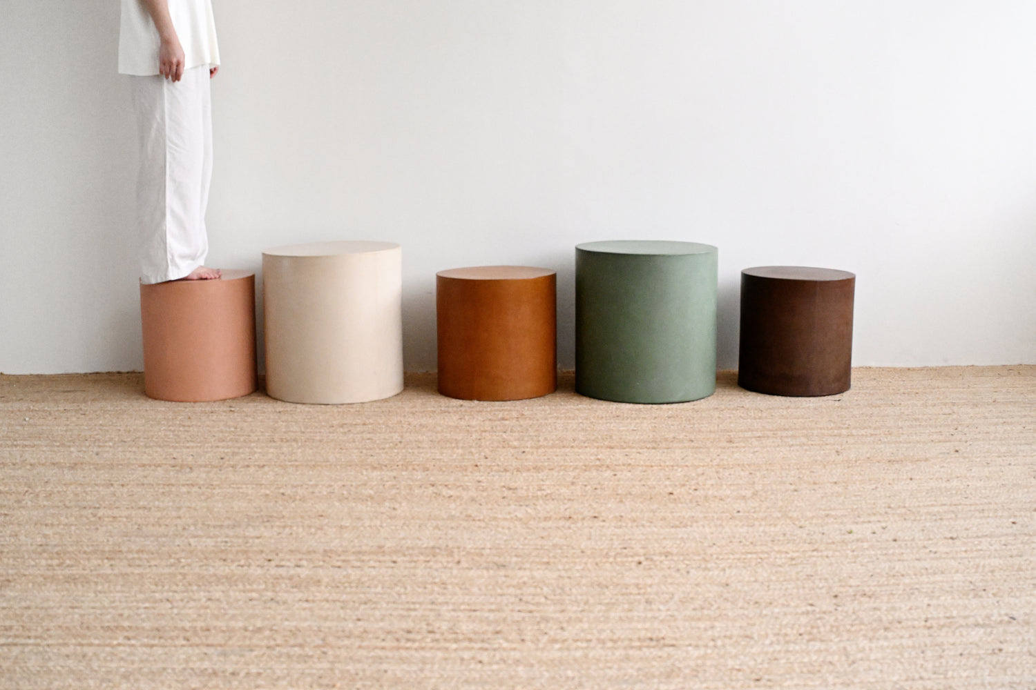 Five cylindrical stools in various colors arranged on a carpeted floor.