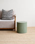 Green stool next to a gray sofa with a striped pillow on a beige carpet.