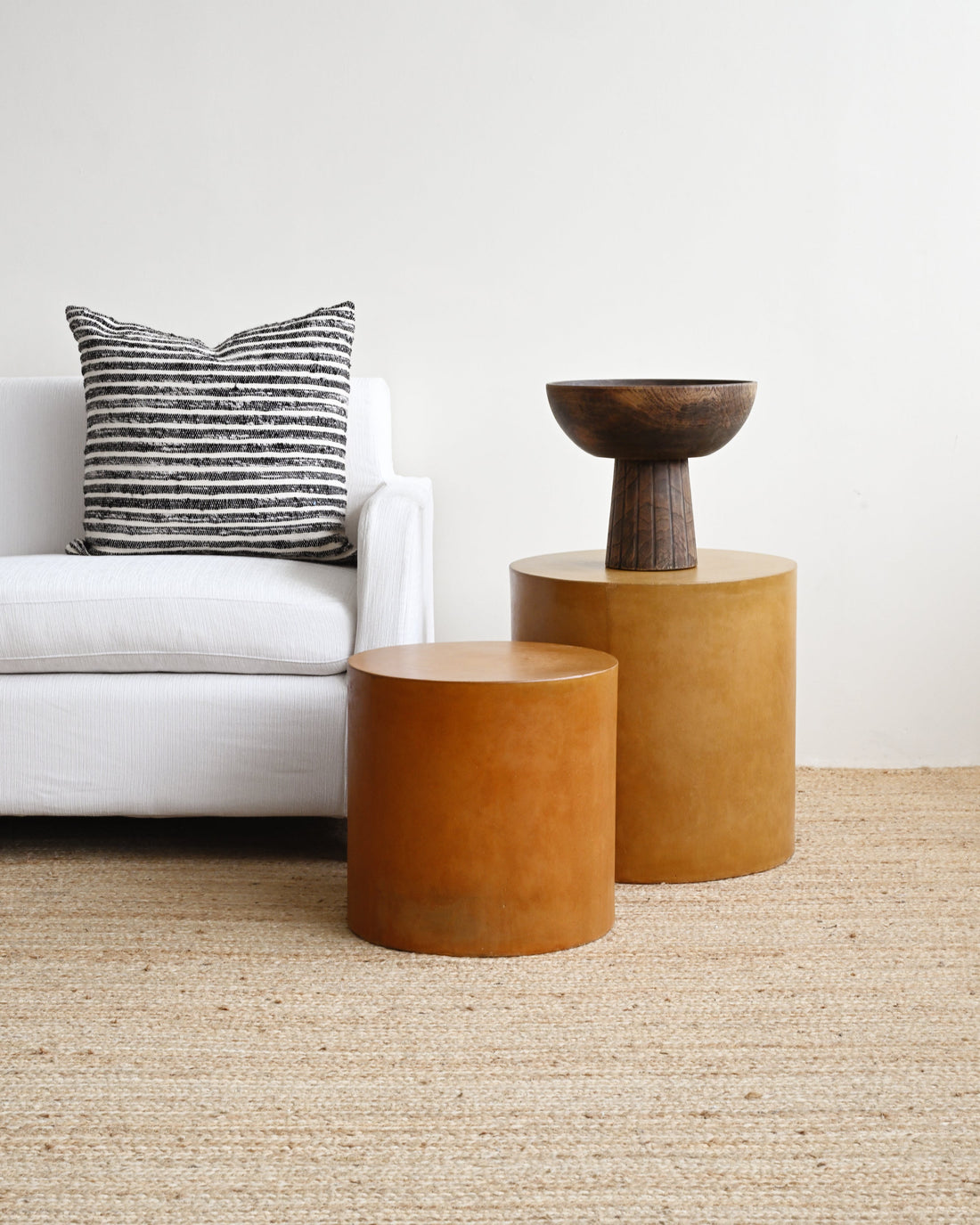 Two brown cylindrical side tables in a living room setting with a white sofa and striped pillow.