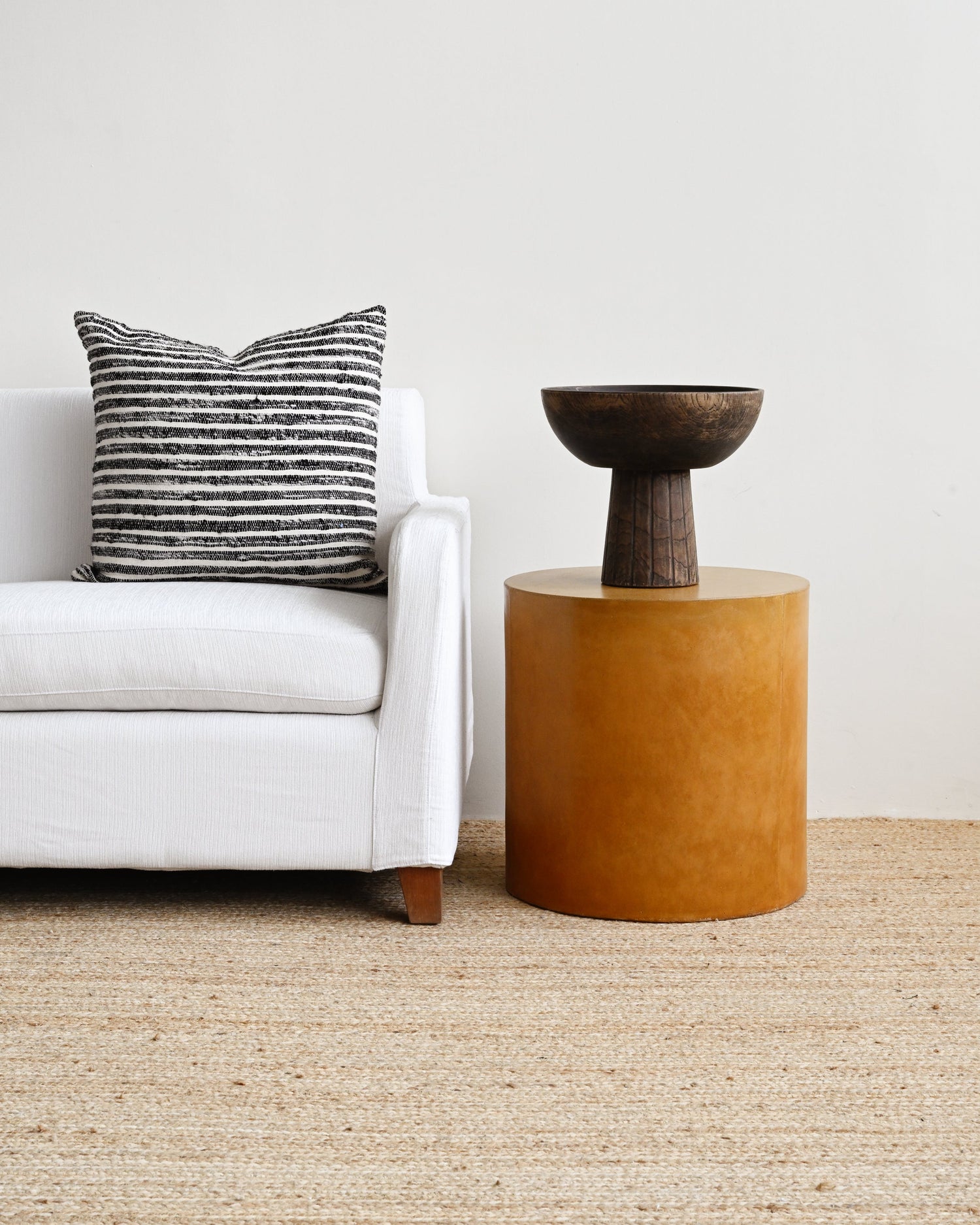 White sofa with a striped pillow and a brown side table in a minimalistic living room.