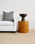 White sofa with a striped pillow and a brown side table in a minimalistic living room.