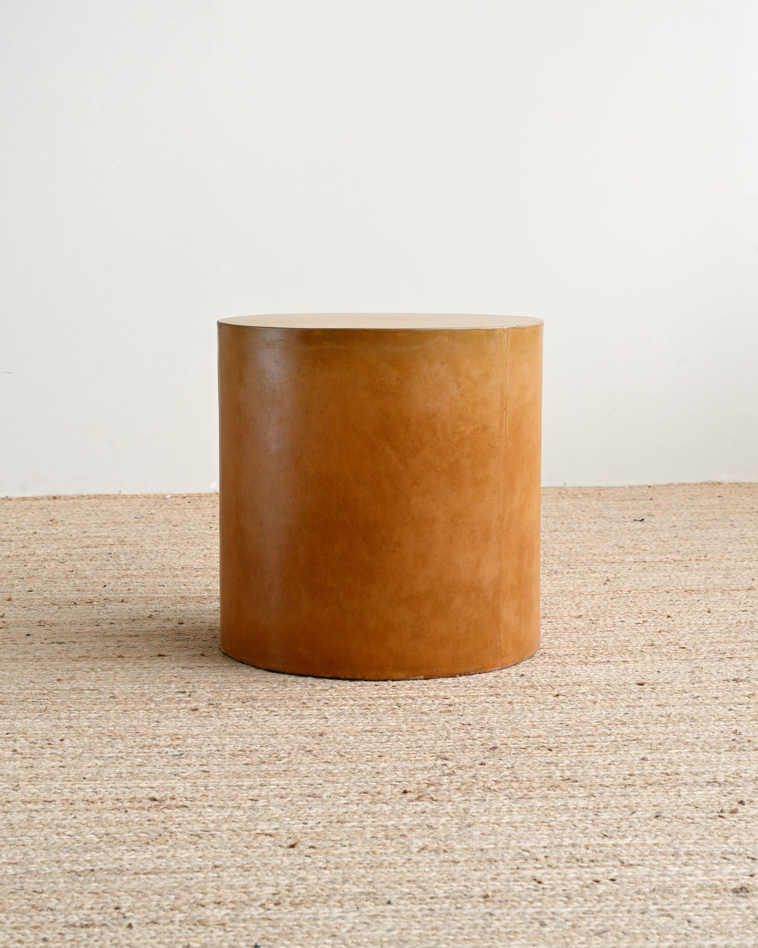 Brown cylindrical stool on a textured beige surface with a white background