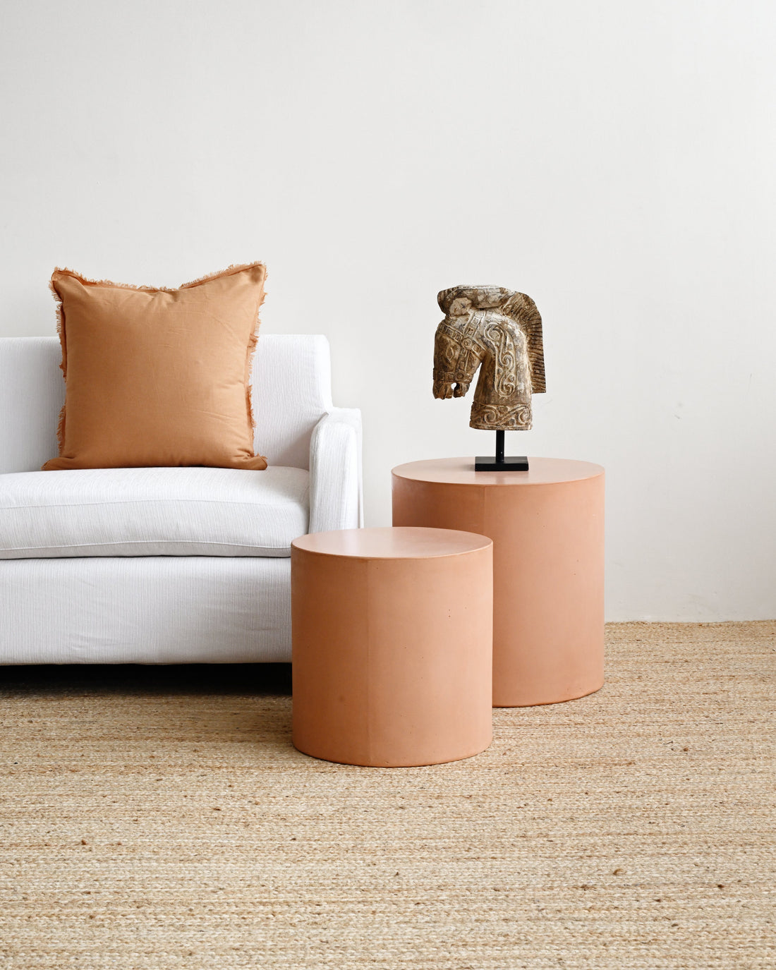 Two terracotta-colored side tables with a decorative horse head sculpture in a living room setting.