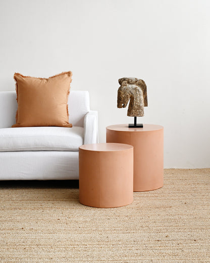 Two terracotta-colored side tables with a decorative horse head sculpture in a living room setting.