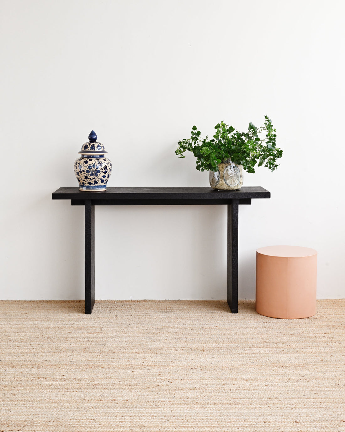 Minimalist room with a black console table, decorative jar, and plant against a white wall.