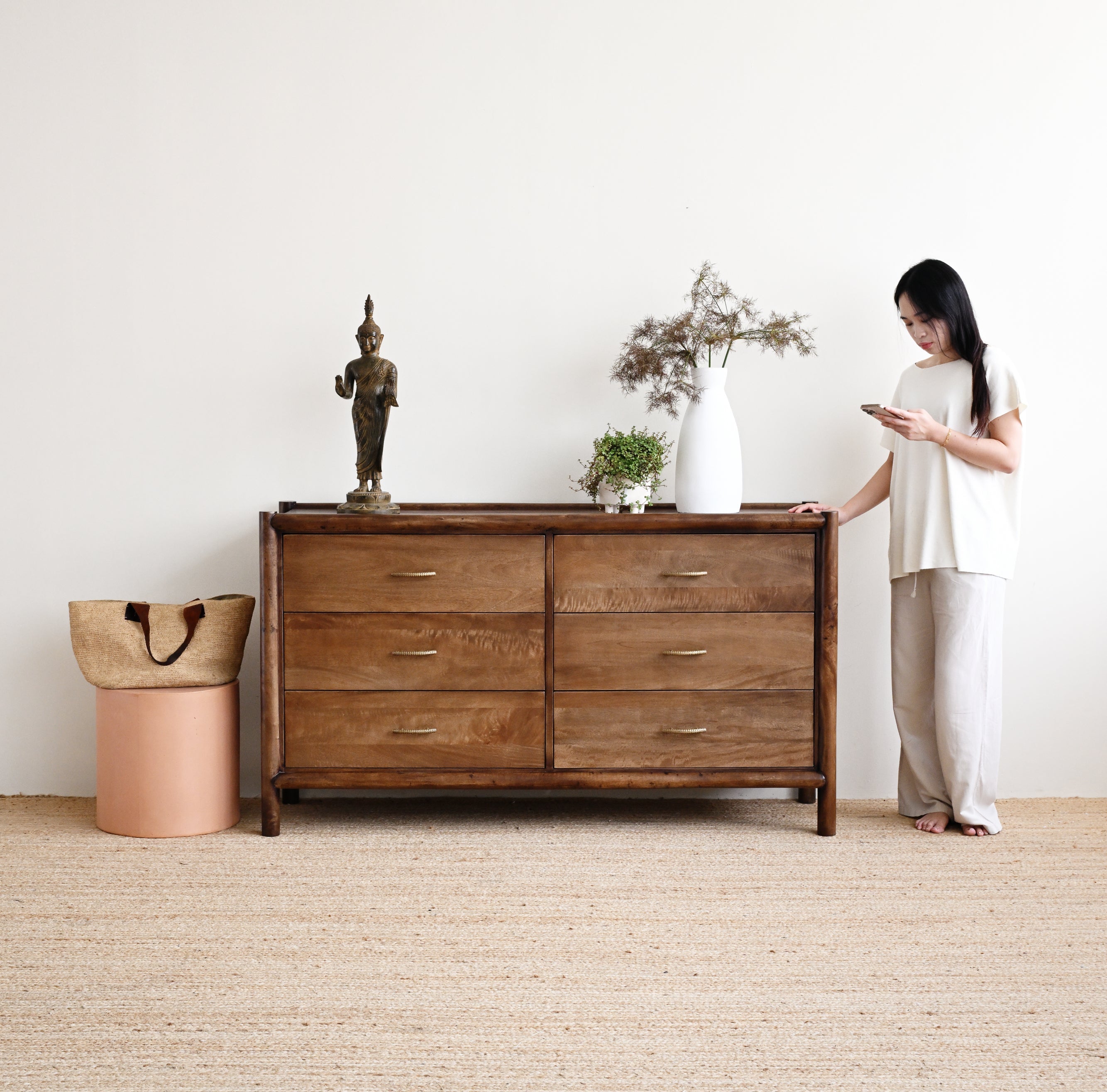 Woman standing next to a wooden dresser in a minimalistic room.
