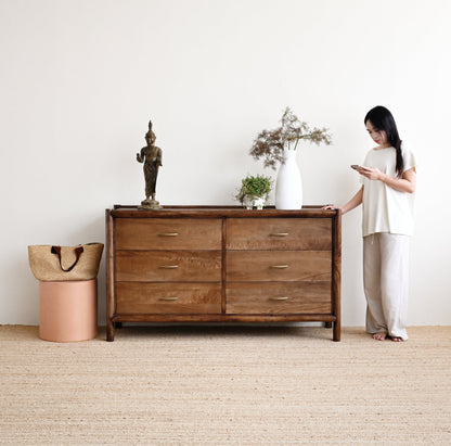 Woman standing next to a wooden dresser in a minimalistic room.