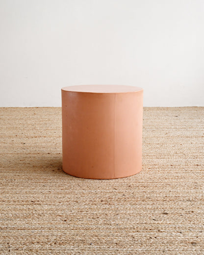 Cylindrical terracotta-colored object on a textured surface with a white background